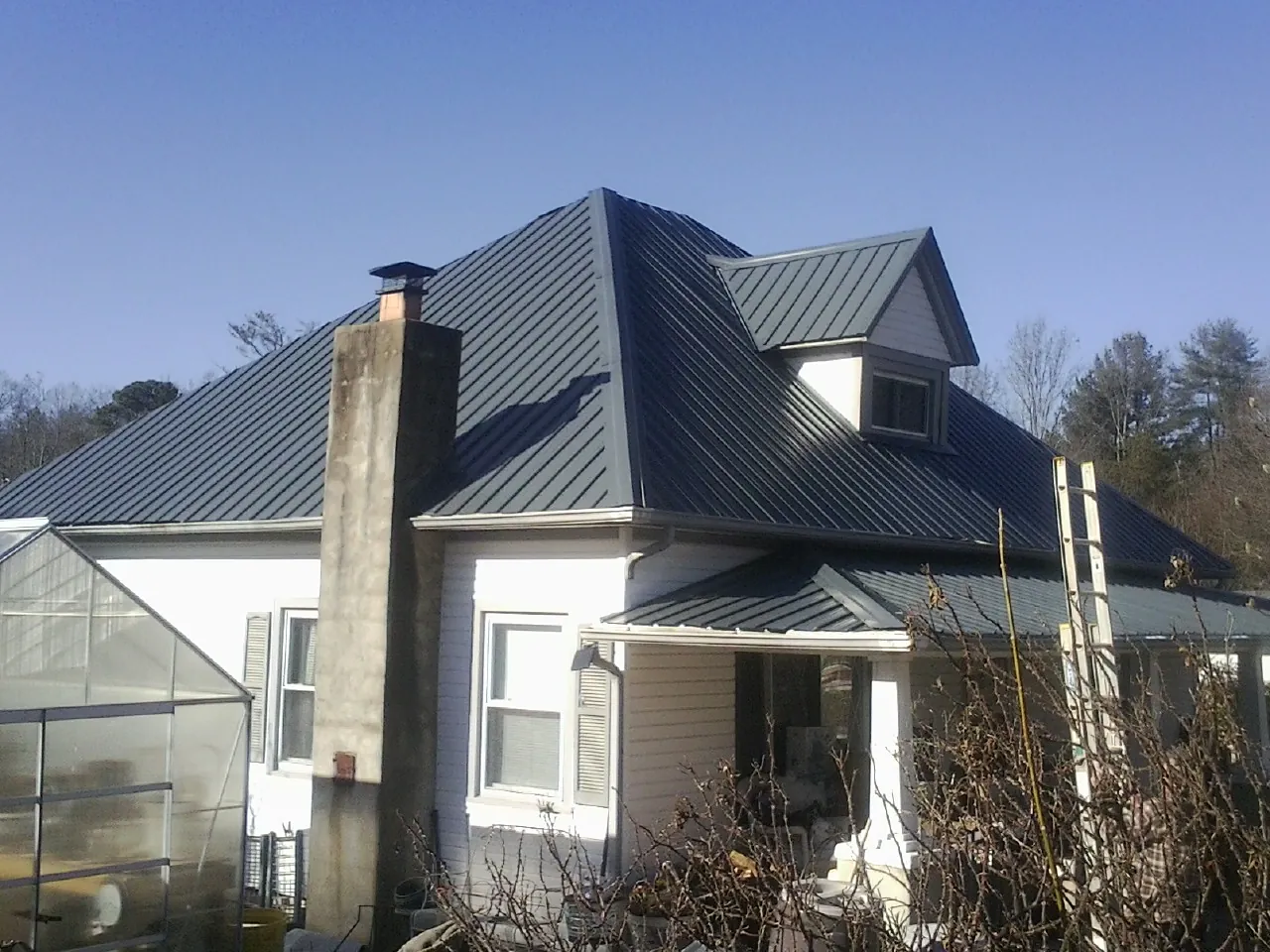 Dark blue standing seam metal roof on a white farmhouse with dormer — Slate & Tile Roof Repair by Roofing Brothers in West Mansfield