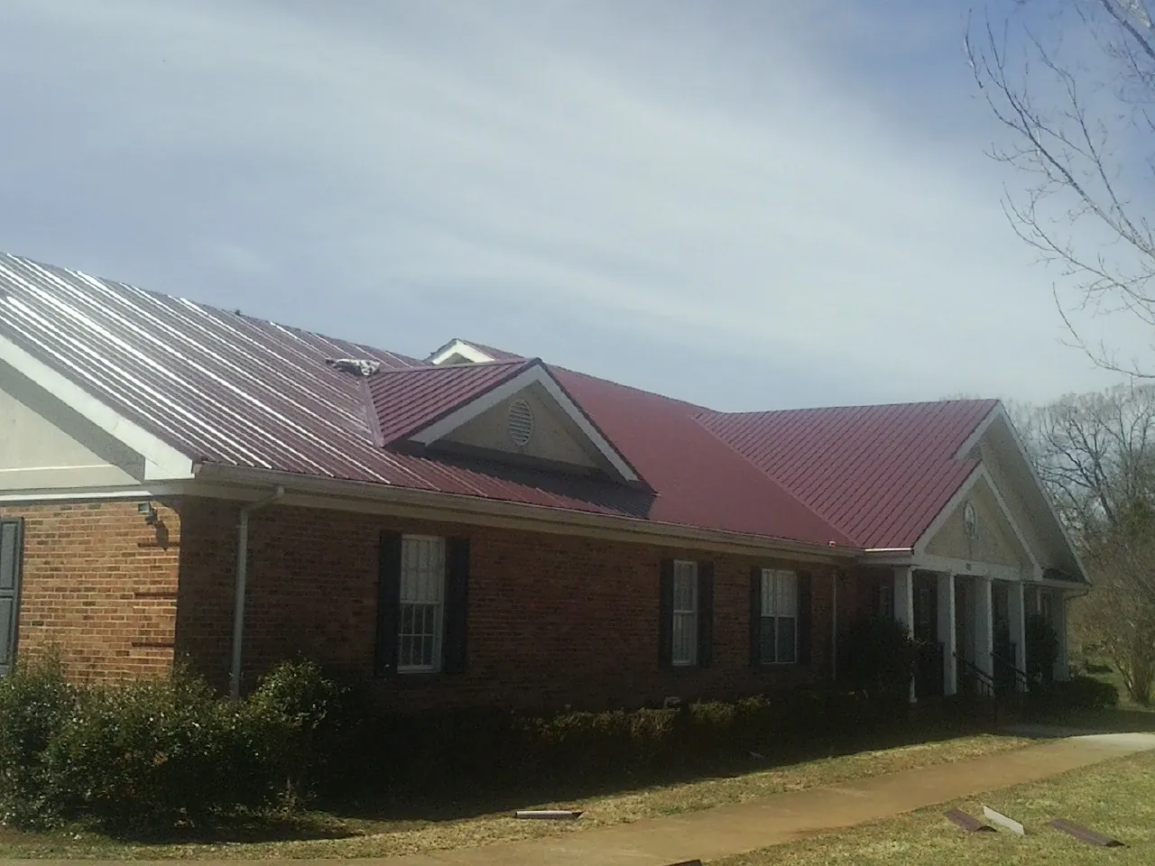 Red metal roof with gabled entries on a long brick building, from a Hail Damage Roof Repair job in West Mansfield