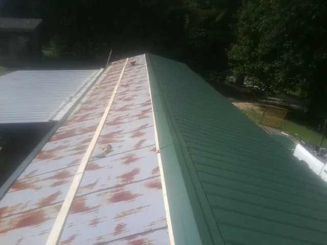 Old rusted panels beside newly installed green metal roofing — Wind Damage Roof Repair by Roofing Brothers in West Mansfield