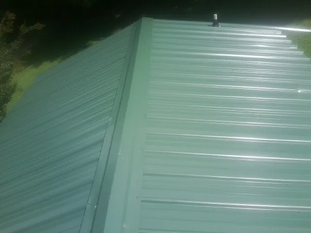New green metal panels meeting at the ridge of a roof in West Mansfield