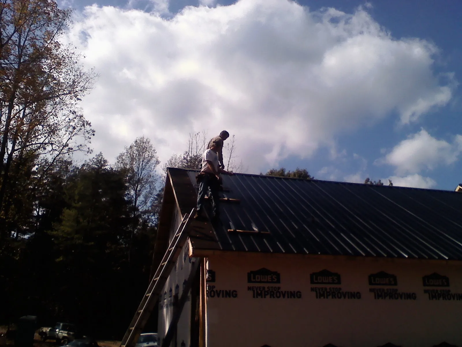 Roofer fastening dark metal panels high against a cloudy sky, from a Roof Inspection job in West Mansfield