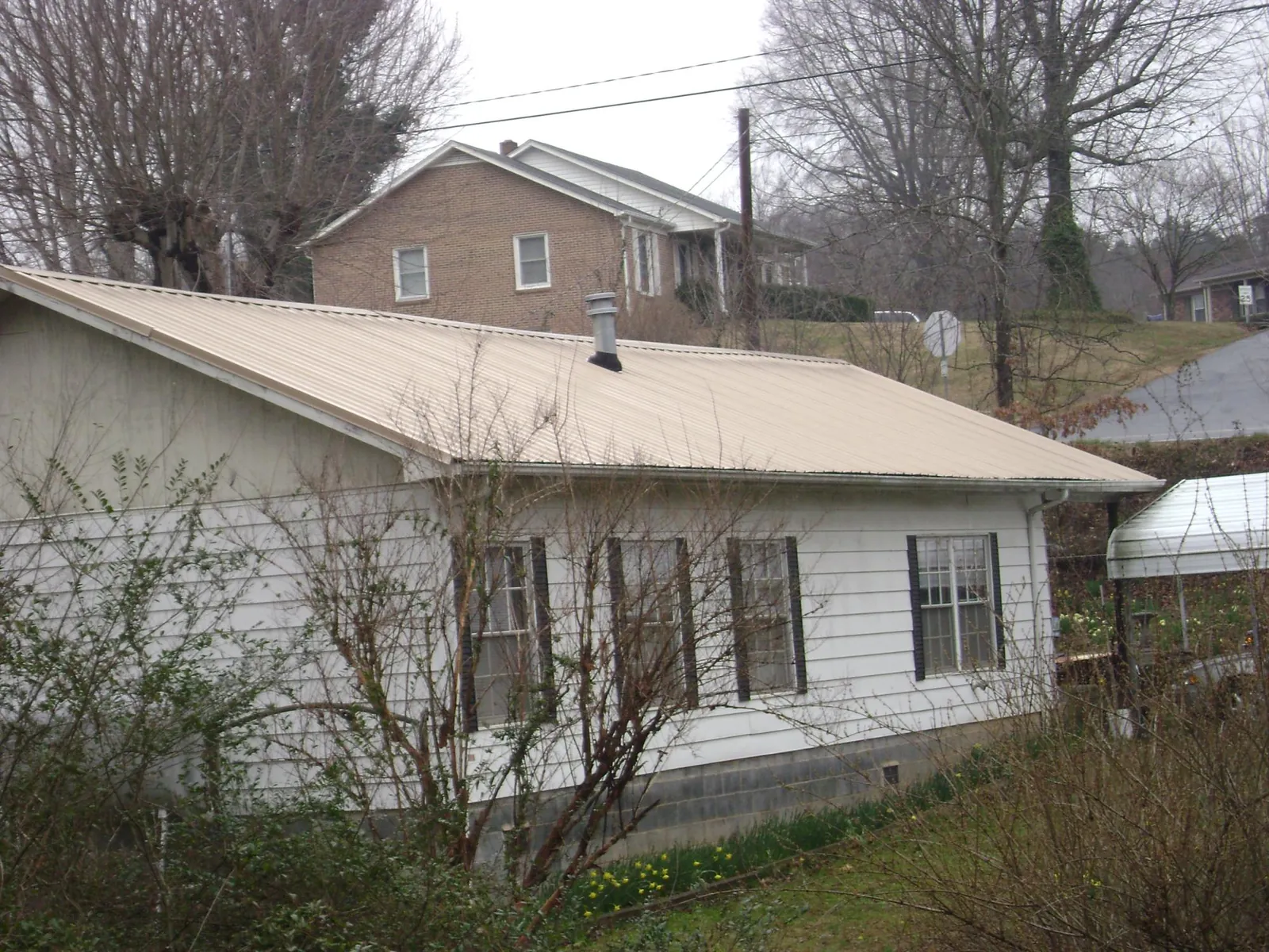 Tan metal roof on a white sided house set into a hillside — Commercial Roofing by Roofing Brothers in West Mansfield