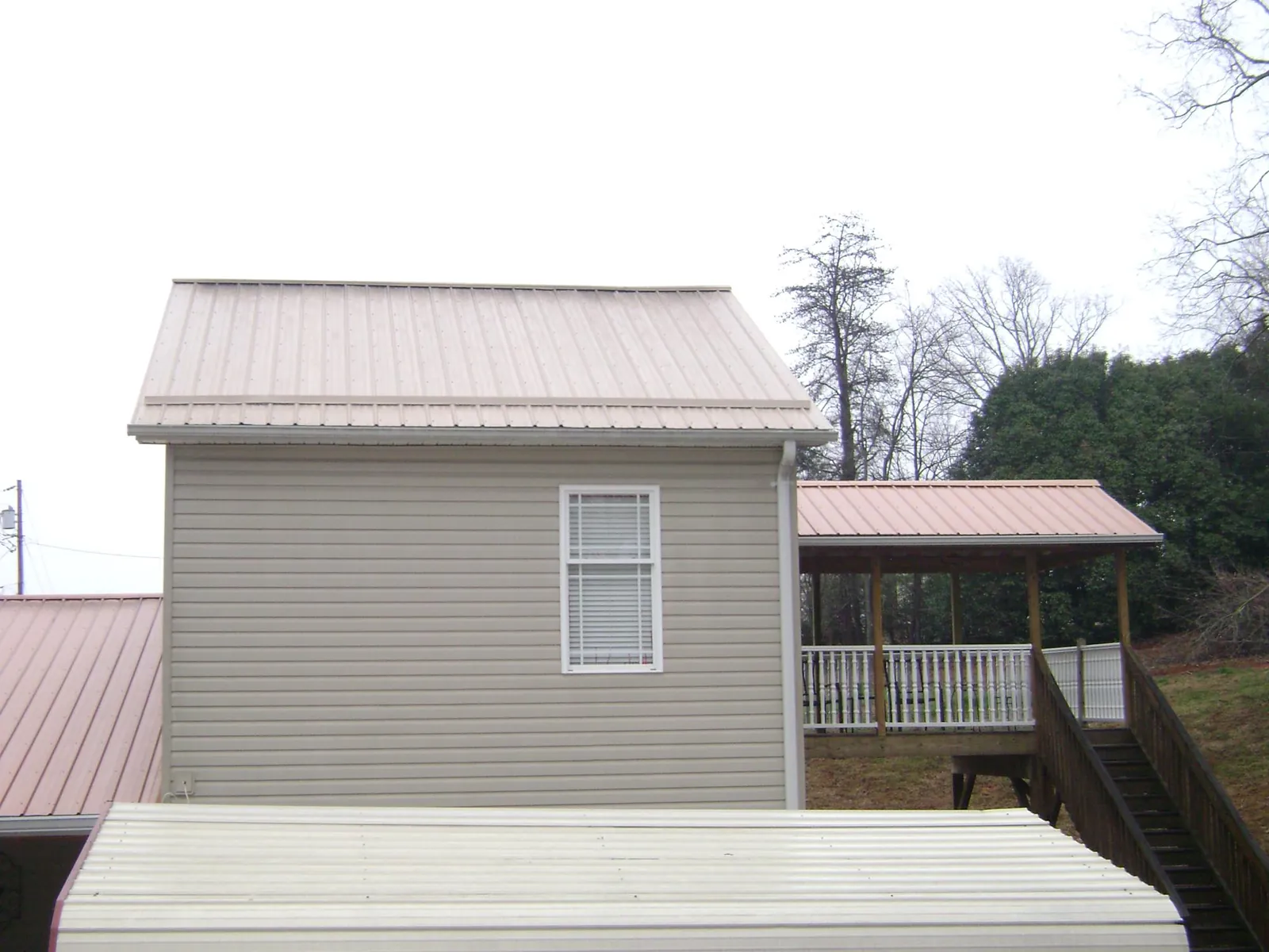 Tan metal roofs on a two story addition and attached porch, from a Roof Replacement job in West Mansfield